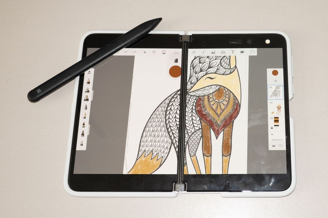 A Surface Duo foldable phone showing Sketchbook full screen and a Surface Pen sitting on the corner of the screen at an angle. The work shown on-screen is a partially complete coloring page.