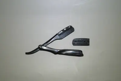 A swappable blade, folding straight razor with the blade compartment open & parts shown